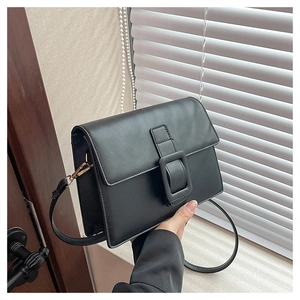 Detail of black crossbody bag with large square buckle and gold hardware accents