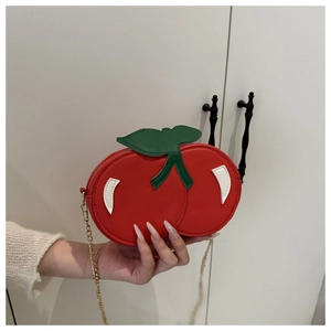 Detail of red cherry crossbody bag showing leaf decor and golden metal chain link