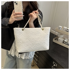 Close-up of white tweed tote bag featuring woven texture and gold chain shoulder strap