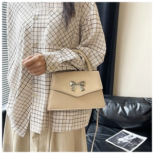 Dettaglio di una borsa beige crema con fiocco in metallo argento indossata da una modella