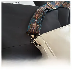 Close-up of beige shoulder bag featuring a colorful patterned strap and gold hardware