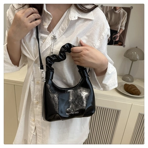 Detail of black patent leather half-moon bag with ruched handle and metal hardware