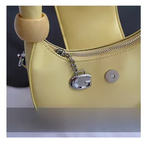 Detail showing the silver G-pendant, zipper, and metal hardware on a yellow leather bag