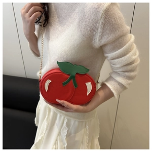 Detail of red cherry shaped shoulder bag with green leaf accents and gold chain strap