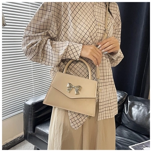 Detailed view of beige crossbody bag with silver bow buckle worn by model