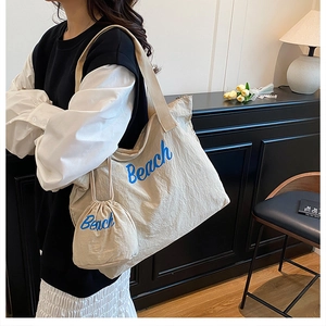 Close-up of a cream-colored drawstring tote bag set with blue Beach script embroidery