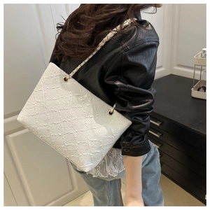 Detail of white quilted tote bag with gold chain strap worn by a model in black leather