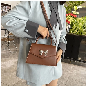 Borsa a trapezio marrone con fiocco dorato portata a spalla in un interno luminoso