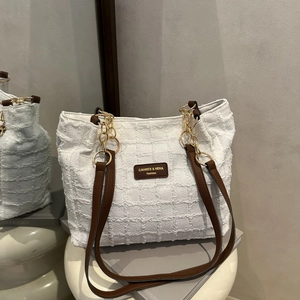 White textured tote bag with chain strap and leather accents on a modern pedestal
