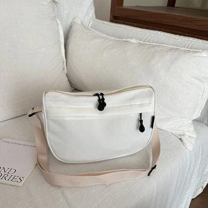 Minimalist white nylon crossbody bag with dual zippers shown on a cozy bedding setup