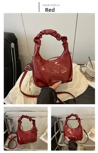 Detail view of red glossy crescent bag featuring pleated handle and fashion logo print