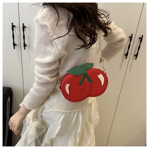Close-up of creative cherry-shaped crossbody bag with gold chain strap on white outfit