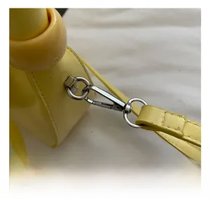 Detail of yellow crossbody bag showing silver metal swivel hook and thin shoulder strap