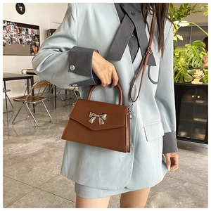 Borsa a tracolla in pelle marrone con fiocco dorato abbinata a un blazer azzurro