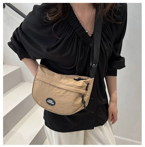 Close-up of khaki nylon crescent crossbody bag worn by model on white stairs
