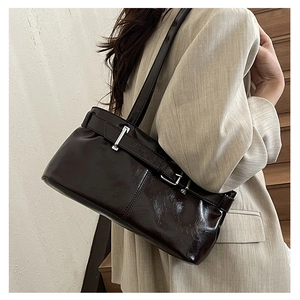 Close-up of dark brown leather underarm bag with silver buckle on a stylish model