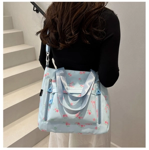Detail of light blue floral tote bag featuring pink rose patterns and dual zipper pockets