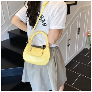 Detail of a bright yellow crescent bag with thick padded handle and metallic spherical buckles