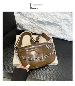 Detail of a brown saddle bag with silver chain and wide woven strap on a white stand