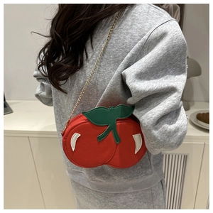 Close-up of a red cherry-shaped shoulder bag with green leaves and a gold chain strap