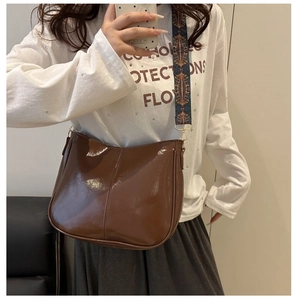 Detail of dark brown patent leather saddle bag with embroidered geometric wide strap