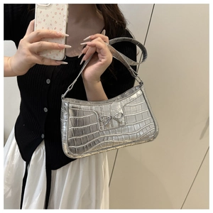 Close-up of silver crocodile embossed texture and metallic bow detail on shoulder bag
