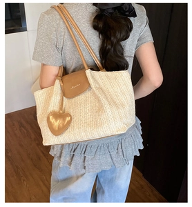 Detail of straw woven tote bag with brown leather flap and heart-shaped pendant charm