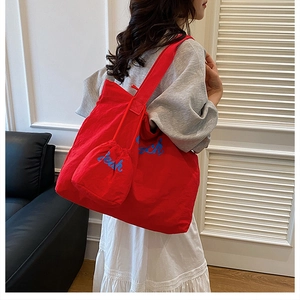 Detail of red nylon tote bag with blue Beach embroidery and matching small zipper pouch