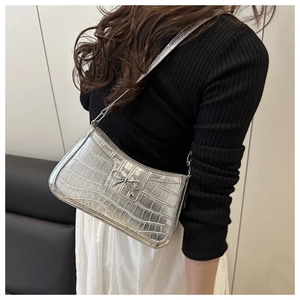 Detail of silver metallic underarm bag featuring crocodile texture and bow decoration