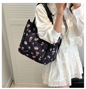 Detail of black floral tote bag with pink blossoms, bow patterns, and wide strap