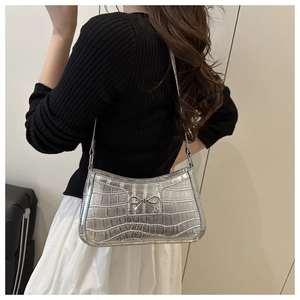 Detail of silver crocodile pattern baguette bag with metallic bow on a black knit outfit