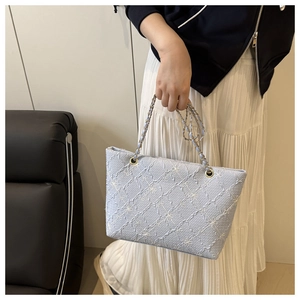 Close-up of light blue tote bag with floral texture and gold chain strap detail