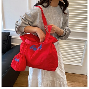 Detail of red large-capacity canvas tote with blue embroidery and matching drawstring bag