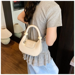 Detail of off-white dumpling bag showing smooth faux leather texture and top handle charm