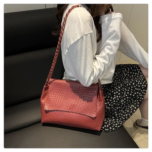 Détail d'un sac à bandoulière tressé rouge avec chaîne dorée porté par un modèle