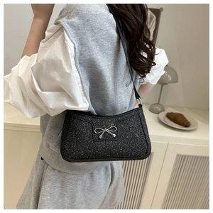 Détail du sac baguette noir scintillant avec nœud argenté porté en sac à bandoulière