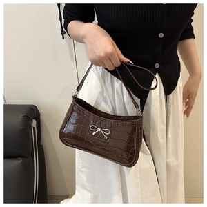 Detail of dark brown faux crocodile baguette bag with a delicate silver metal bow accent