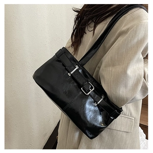 Close-up of black glossy leather underarm bag with decorative silver buckle details