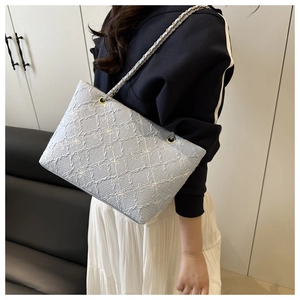 Detail of light blue crossbody bag featuring floral embroidery and leather chain strap