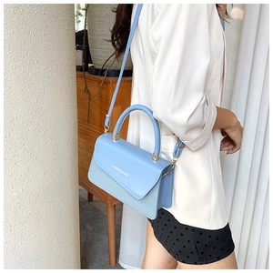 Detail view of light blue crossbody bag with woven texture and gold fashion lettering