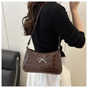 Detail of dark brown crocodile pattern leather shoulder bag with silver bow accent