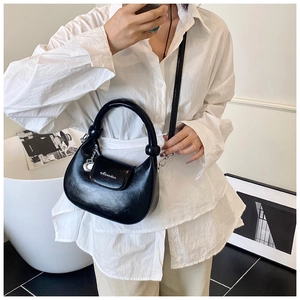 Side view of a glossy black crescent handbag featuring a silver charm and curved handle