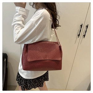 Gros plan d'un sac bandoulière bordeaux tressé avec détail de bandoulière chaîne
