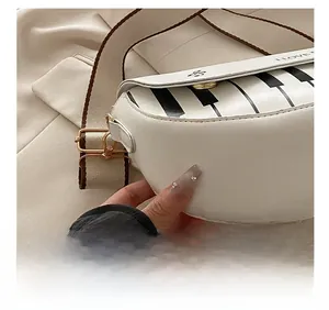 Détail du sac bandoulière blanc en demi-lune avec motif touches de piano et boucle dorée