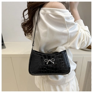 Close-up of black faux crocodile leather shoulder bag with a silver bow detail