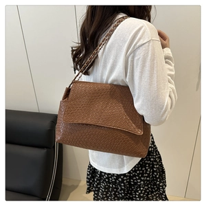Détail d'un sac bandoulière marron tressé avec chaîne porté par une femme mannequin