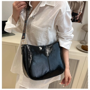 Close-up of black patent leather hobo bag with vintage jacquard wide shoulder strap