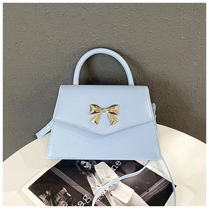 Close-up of a light blue handbag featuring a gold bow buckle on a minimalist white table