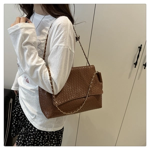 Détail d'un sac à bandoulière en cuir tressé marron avec chaîne dorée sur modèle