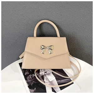 Detail view of beige crossbody bag with gold bow clasp and sleek leather handle